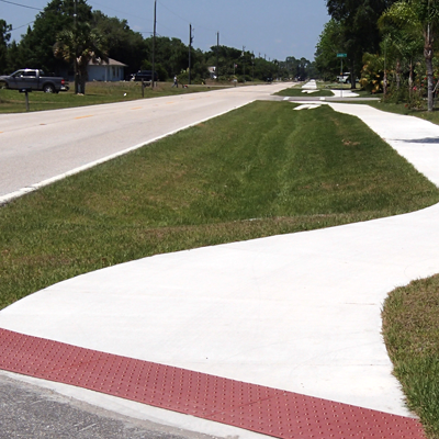 Sidewalk with red tactile paving, a grassy median, and a road.