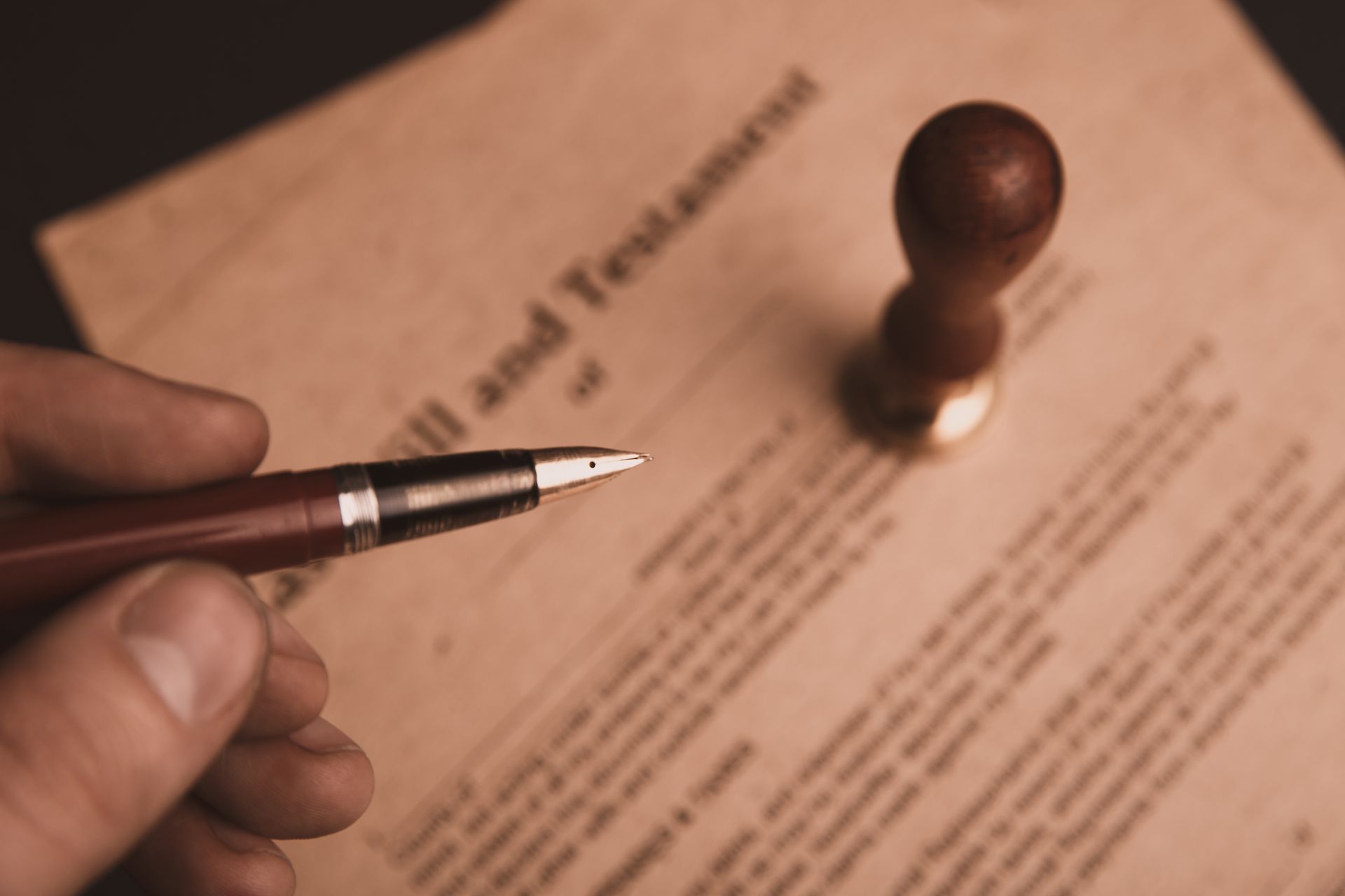 Hand holding pen over a Will and Testament document, with a stamp in the background.