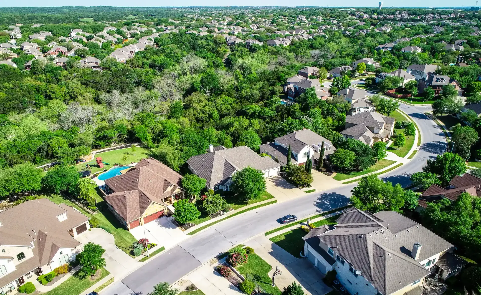 Aerial view of suburban homes, green trees, and winding streets.