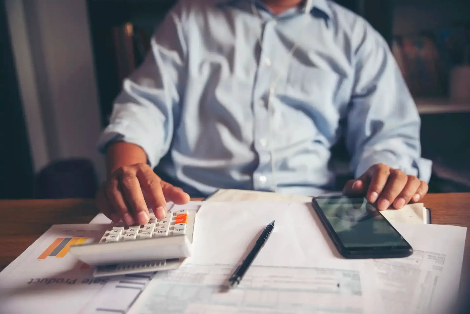 Person in suit calculating with calculator, holding money, at desk.