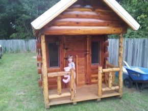 A little girl is standing in front of a wooden playhouse