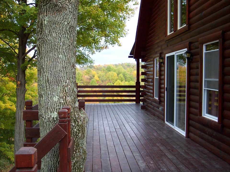 A log cabin has a large deck with a view of the woods
