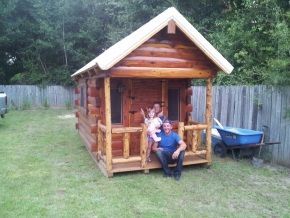A man and two children are sitting on a porch of a log cabin.