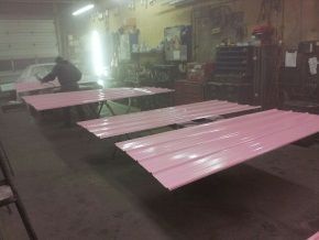 A man is painting pink sheets of metal in a garage.