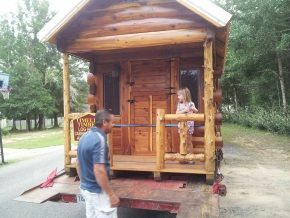 A man and a little girl are standing in front of a small log cabin.