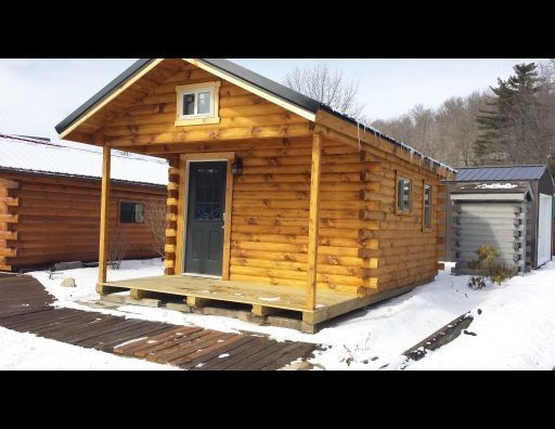 A small log cabin is sitting in the snow next to a garage.
