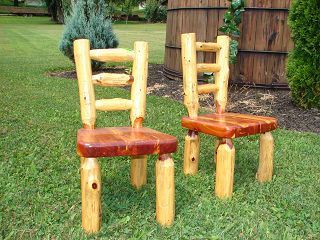 Two wooden chairs made out of logs are sitting in the grass.