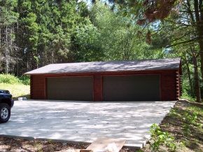 A large garage with three garage doors is in the middle of a forest.