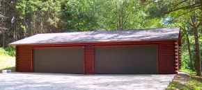 A red garage with two garage doors is in the middle of a forest.