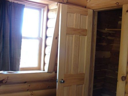 A wooden door is open in a log cabin next to a window.