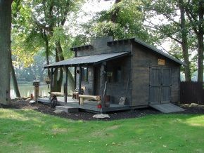 A small wooden shed with a porch and trees in the background