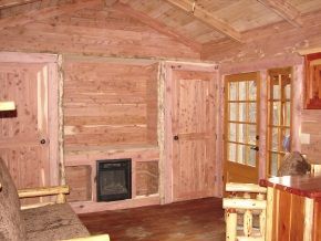 A living room in a log cabin with a couch , chairs , and a fireplace.