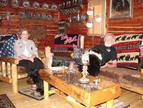 A man and a woman are sitting in a living room in a log cabin.
