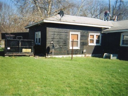 A black house with a dumpster in front of it