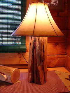 A lamp made out of a log is sitting on a table in front of a window.