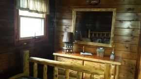 A bedroom in a log cabin with a bed , dresser , mirror and lamp.