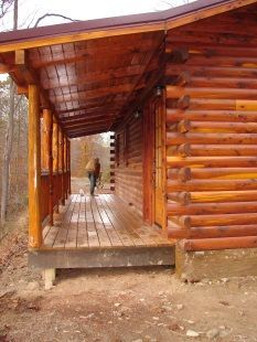 A person is standing on a porch of a log cabin.