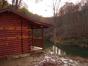 A log cabin is sitting next to a river in the woods.