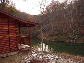 A log cabin is sitting next to a river in the woods.