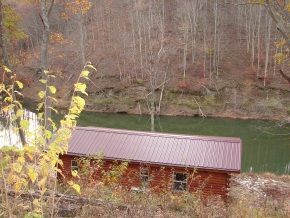 A log cabin is sitting next to a river in the woods.