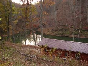 A log cabin is sitting next to a river in the woods.