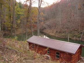 A log cabin is sitting next to a river in the woods.