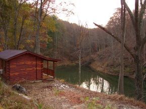 A log cabin is sitting next to a river in the woods.
