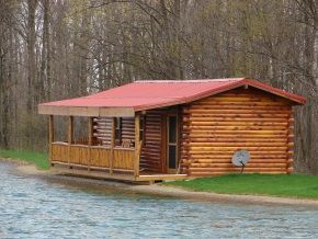 A small log cabin with a red roof is sitting on the shore of a lake.