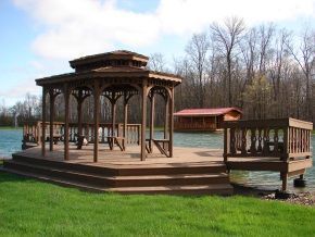 A wooden gazebo is sitting on top of a wooden deck next to a lake.