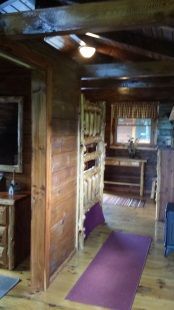 A living room in a log cabin with a bunk bed and a purple rug.