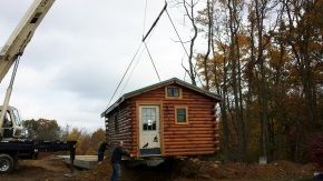 A crane is lifting a small log cabin into the air.