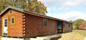 A log cabin with a green roof is sitting in the middle of a field.
