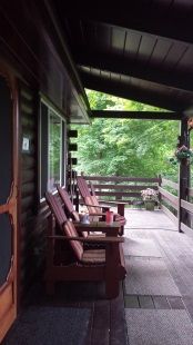 There are many chairs on the porch of a log cabin.