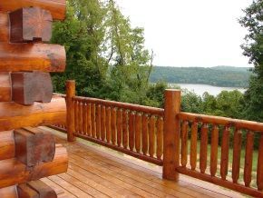 A log cabin with a wooden deck and railing overlooking a lake.