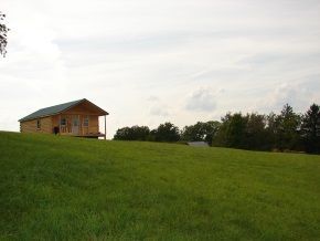 A small wooden house is sitting on top of a grassy hill.