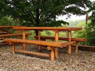 A wooden picnic table is surrounded by trees and gravel