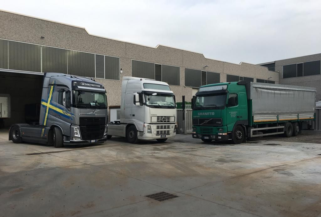 Un carrello elevatore carica un grande oggetto metallico su un camion Volvo argento e blu all'interno di una fabbrica.