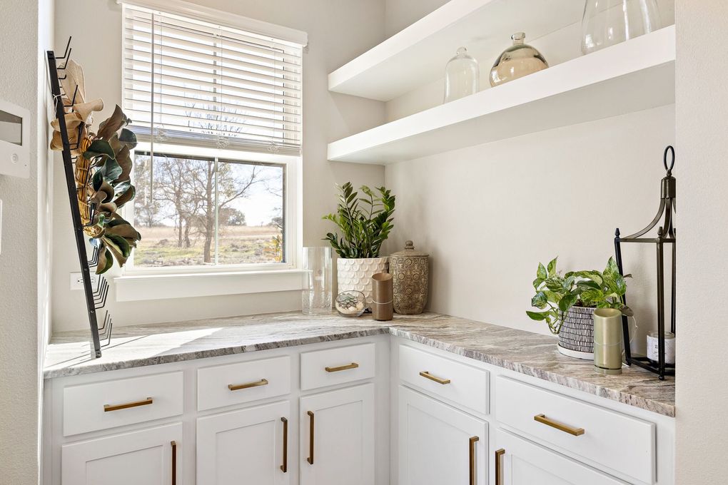 A laundry room with white cabinets , granite counter tops , a sink and a window.