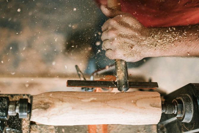 Hands turning a wood lathe as wood shavings fly off a spinning log