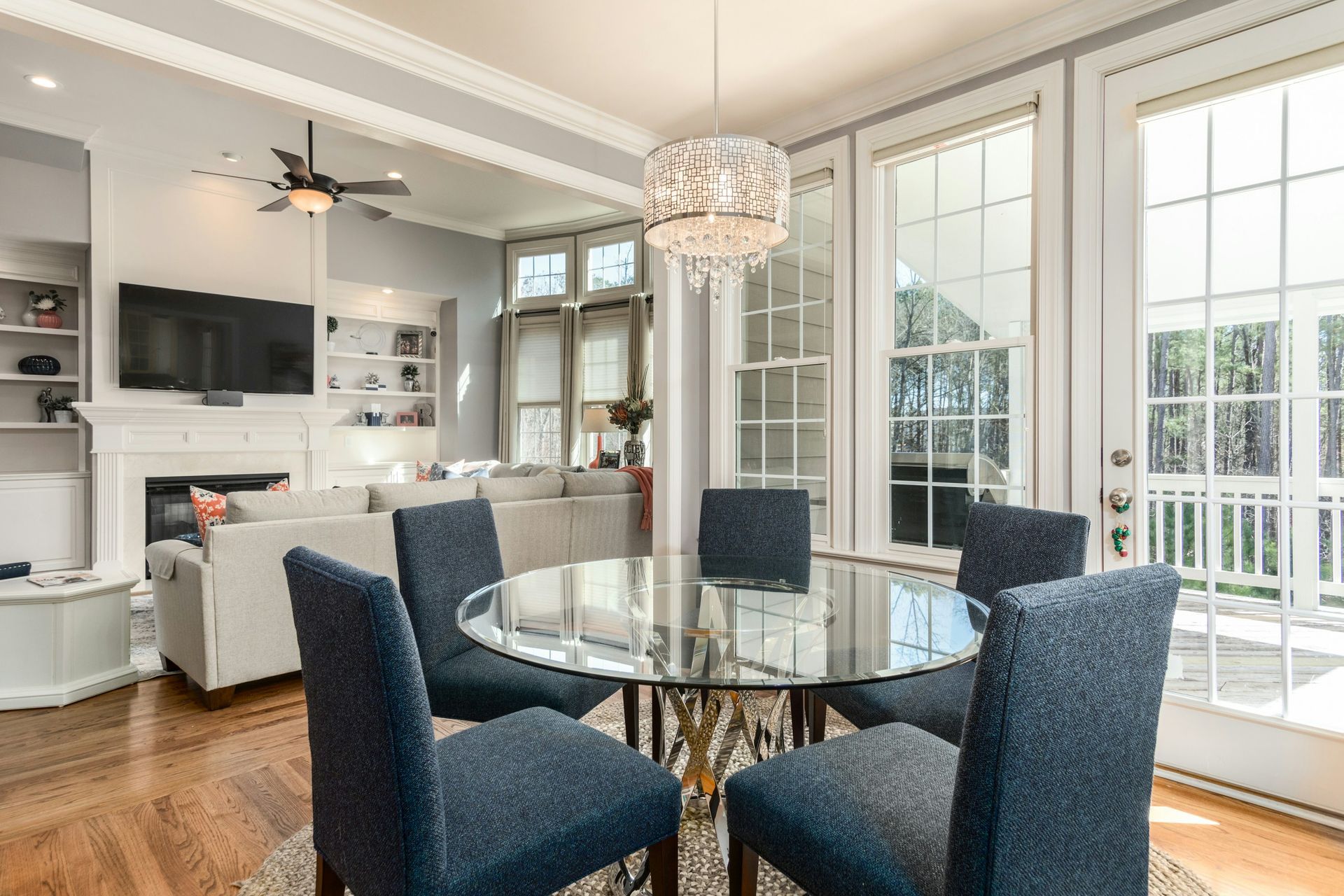 Bright dining room with glass table, navy chairs, chandelier, and large windows overlooking a deck
