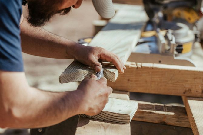 Person sanding a wooden plank at a workbench with a power tool in a woodworking shop