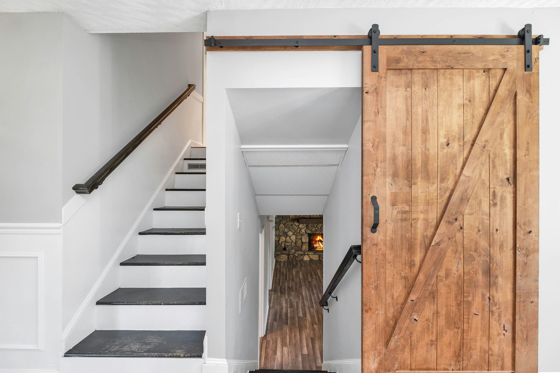 Staircase with a rustic sliding barn door in a white interior hallway