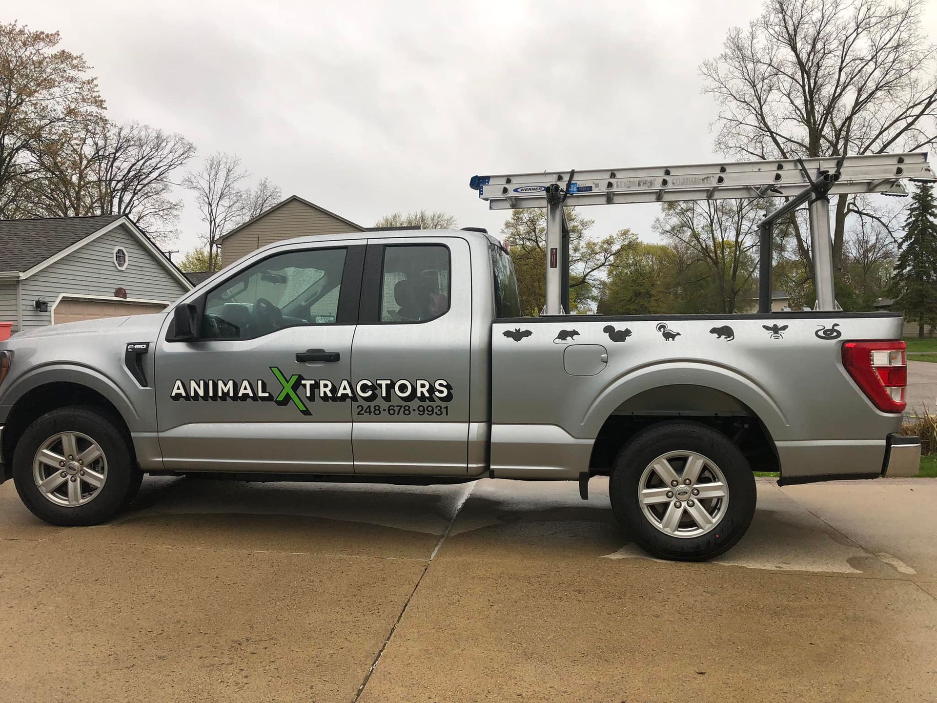 A silver truck with animal tractors written on the side is parked in a driveway.