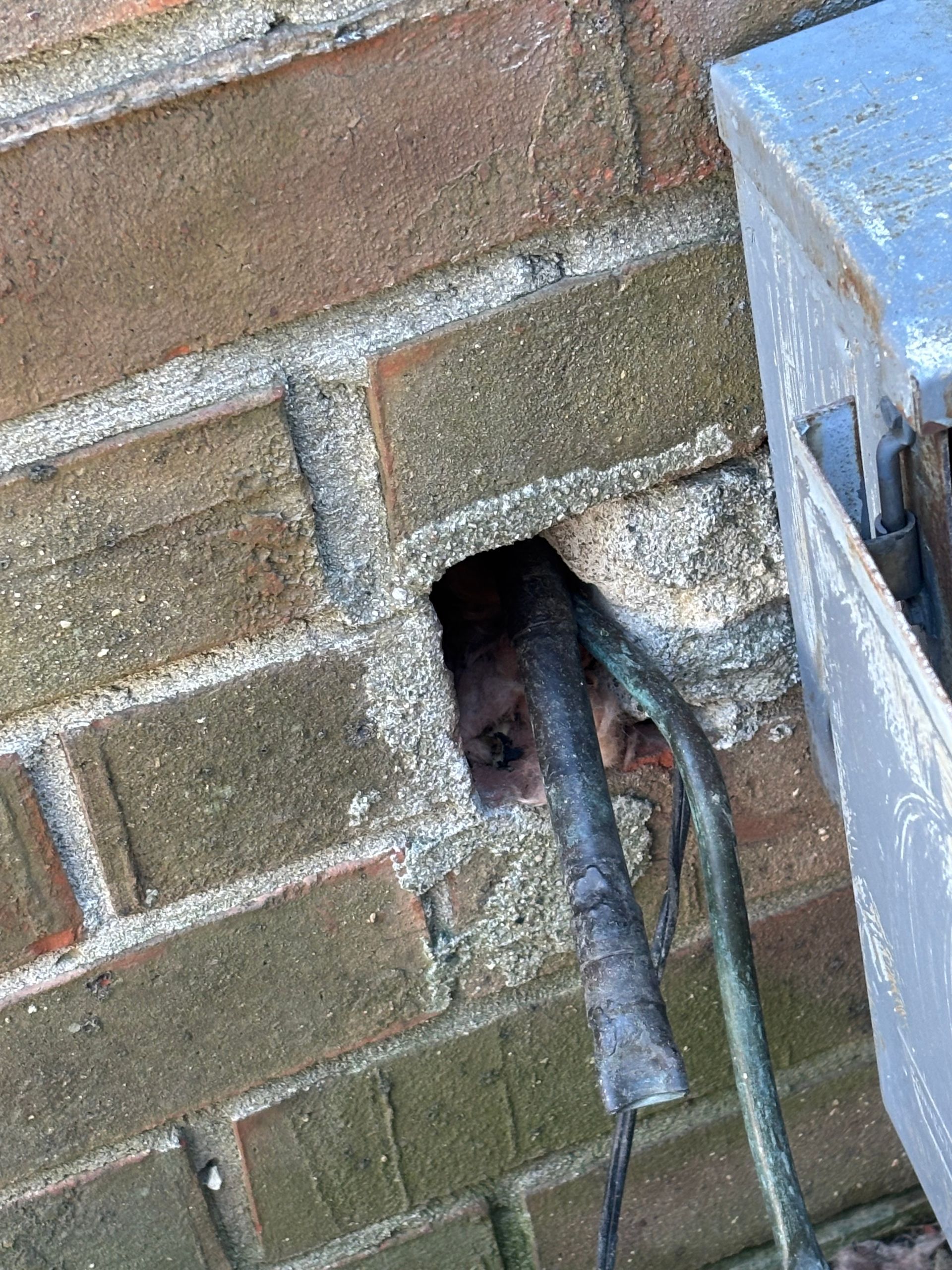 A brick wall with a hole in it and a wire sticking out of it.