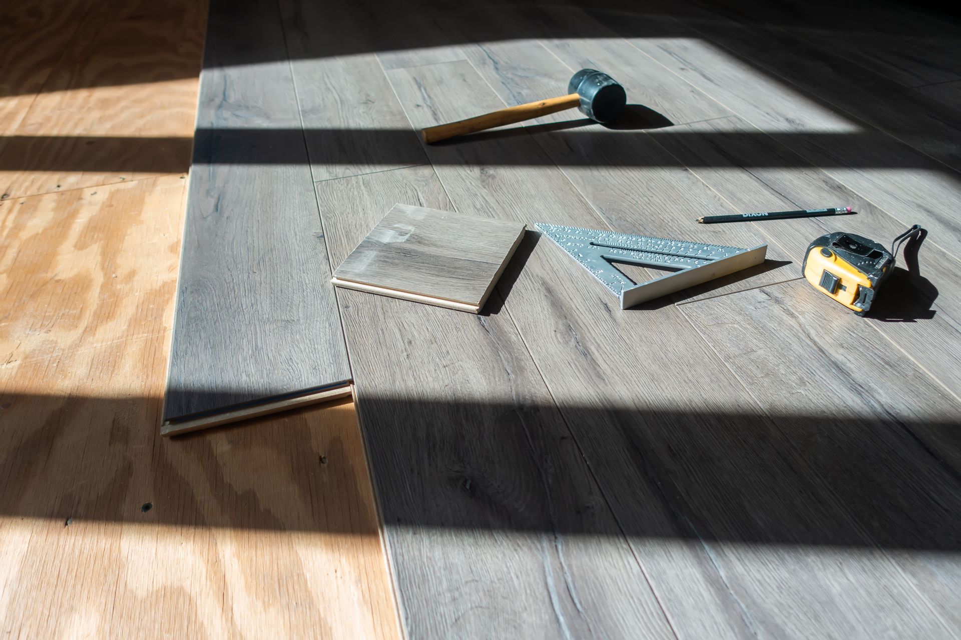 A hammer , ruler , and square are laying on a wooden floor.