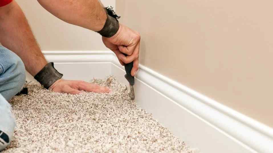 A man is laying carpet on the floor in a room.