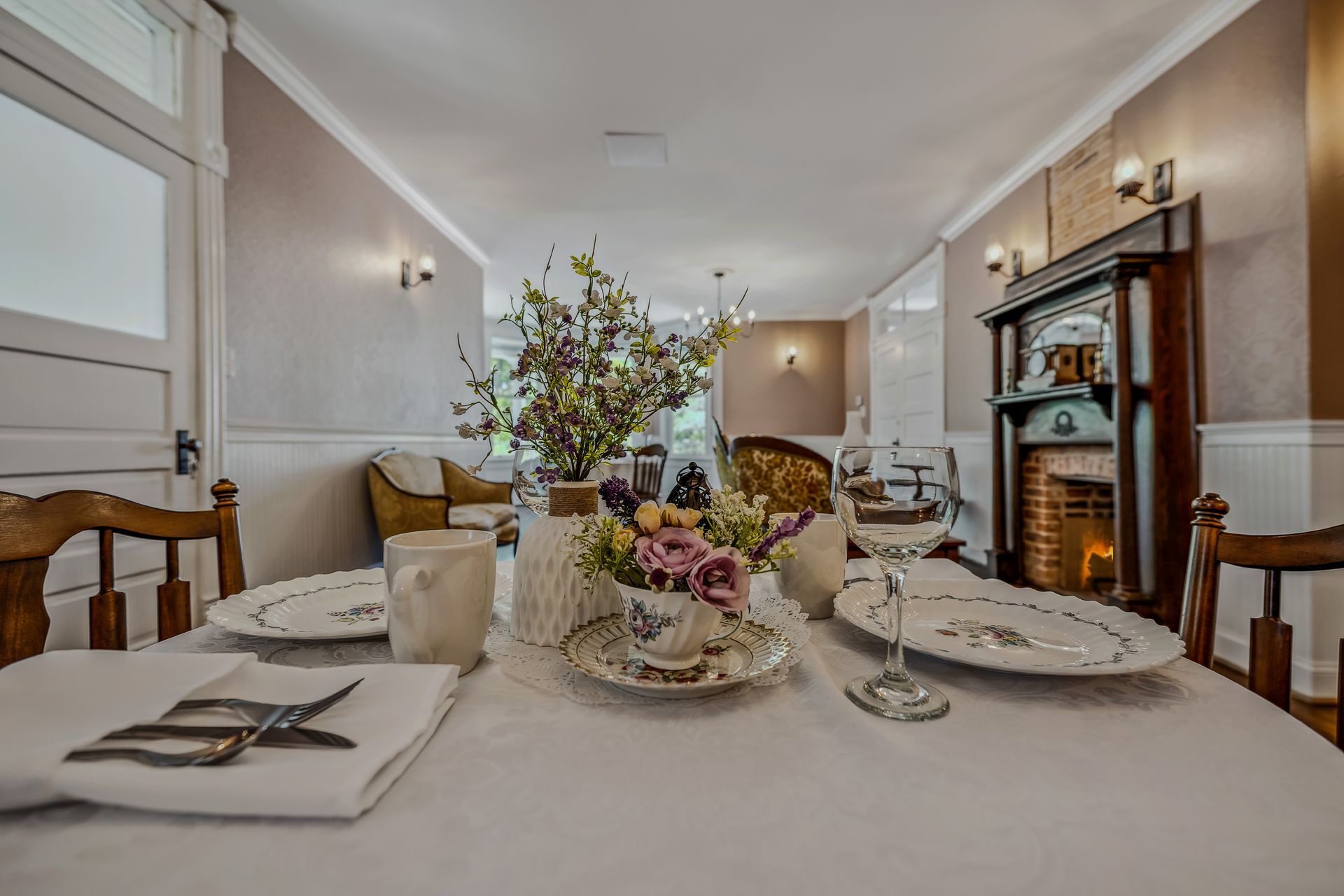 A dining room table with plates , cups , glasses and a vase of flowers on it.