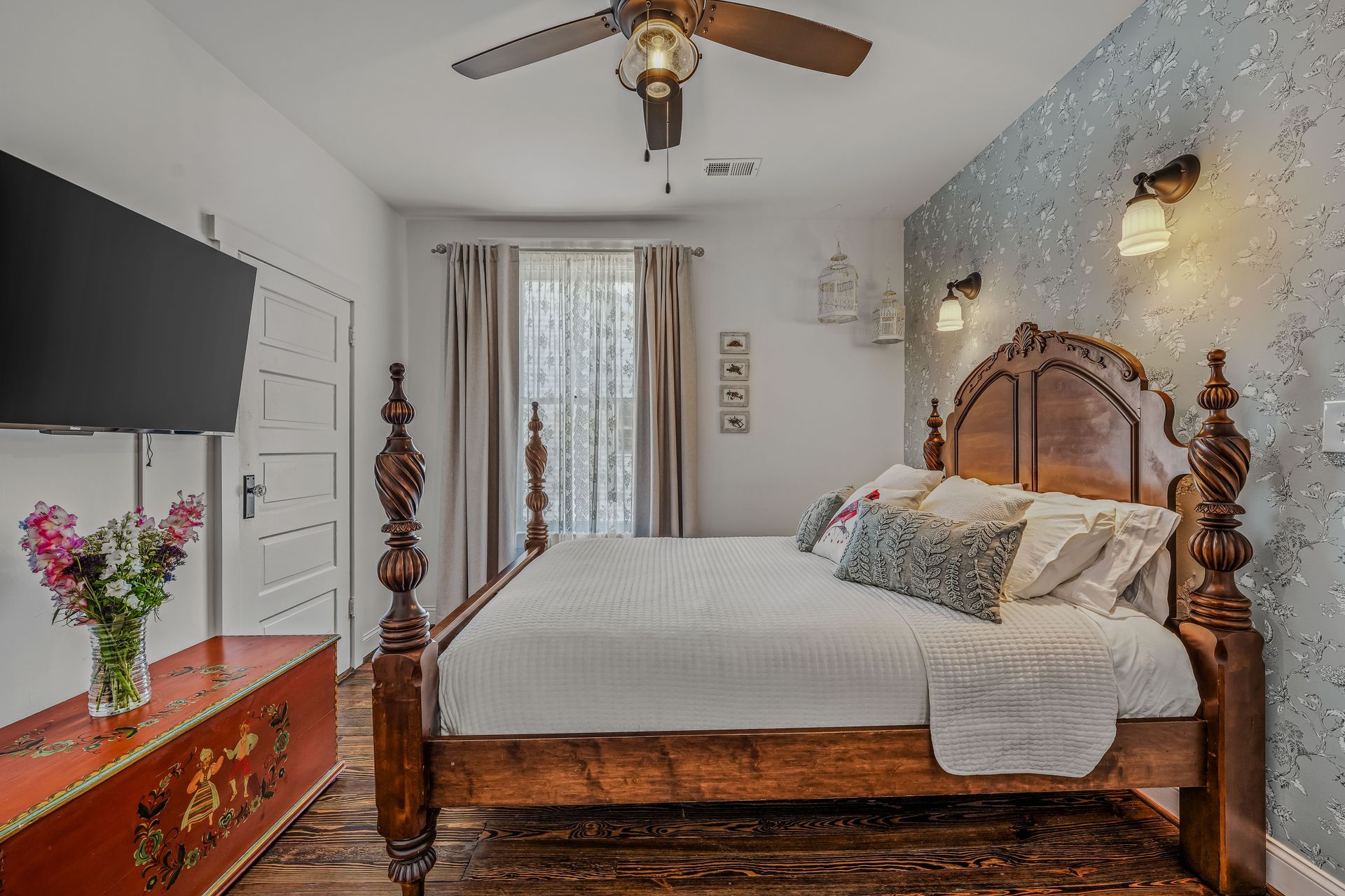 A bedroom with a bed , ceiling fan , television and a large window.
