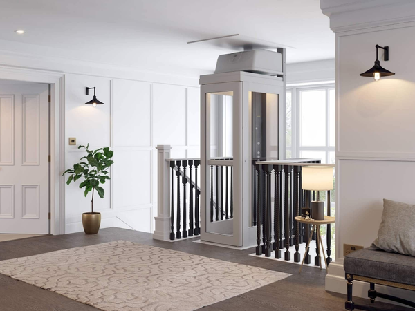A white home elevator installed in an interior hallway, adjacent to a wooden staircase, a lamp, and a potted plant.