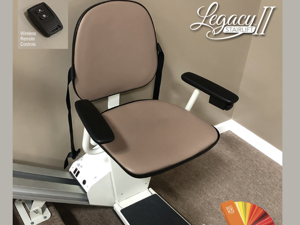 A Legacy II stairlift with a beige seat and armrests installed on a track, featuring a wireless remote control.